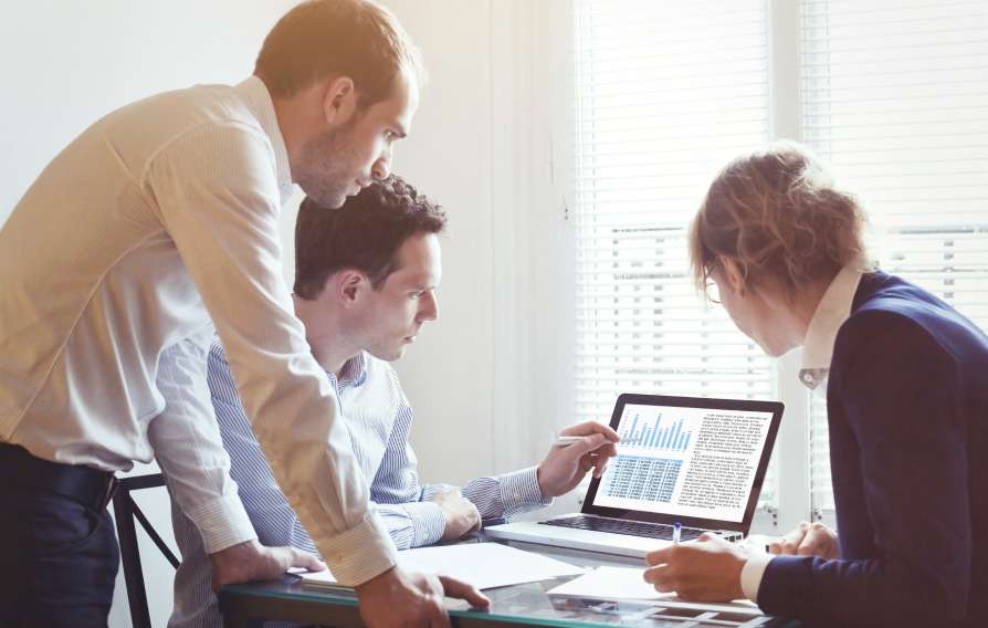 a group of three people looking at a chart on a computer