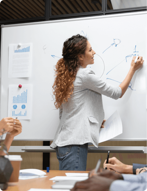 curly-haired woman in white blazer writing on white board